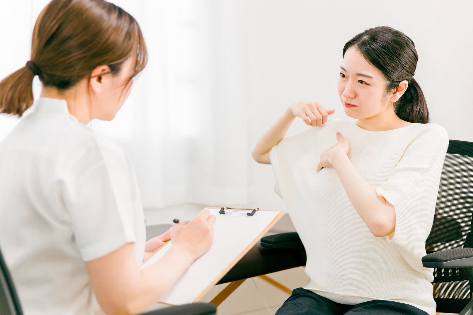 セラピストが、いすに座ったお客様の肩のつらさを聞きながら、用紙に書きとめている