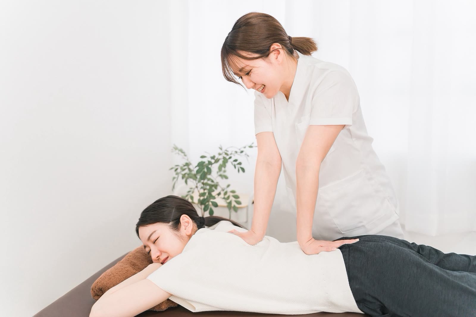 うつ伏せで目を閉じ、気持ちよさそうにほほえむお客様の背中を、セラピストがほぐしている