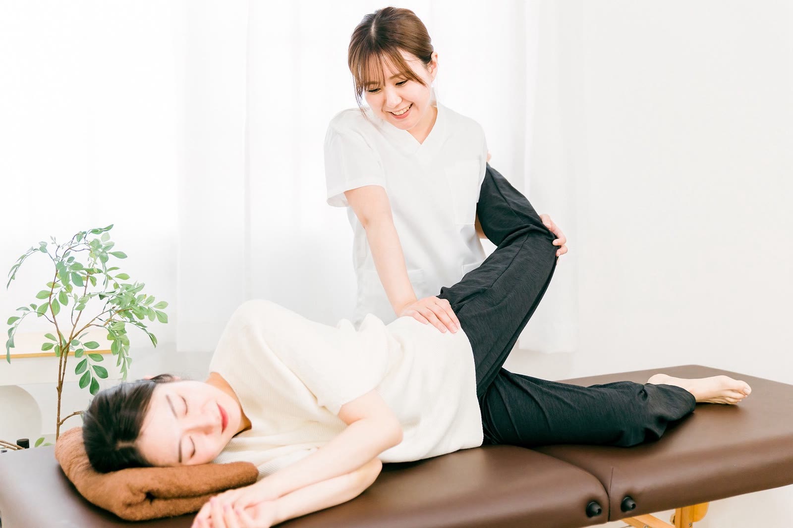 横向きに寝たお客様の脚をセラピストがのばしている。お客様は目を閉じてくつろいでいる